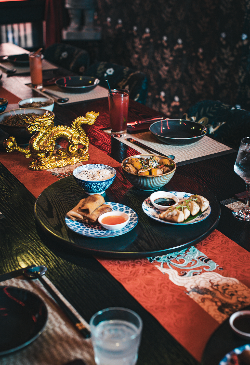 Round dining table set for a meal with Asian-style dishes, bowls, and a gold dragon centerpiece.