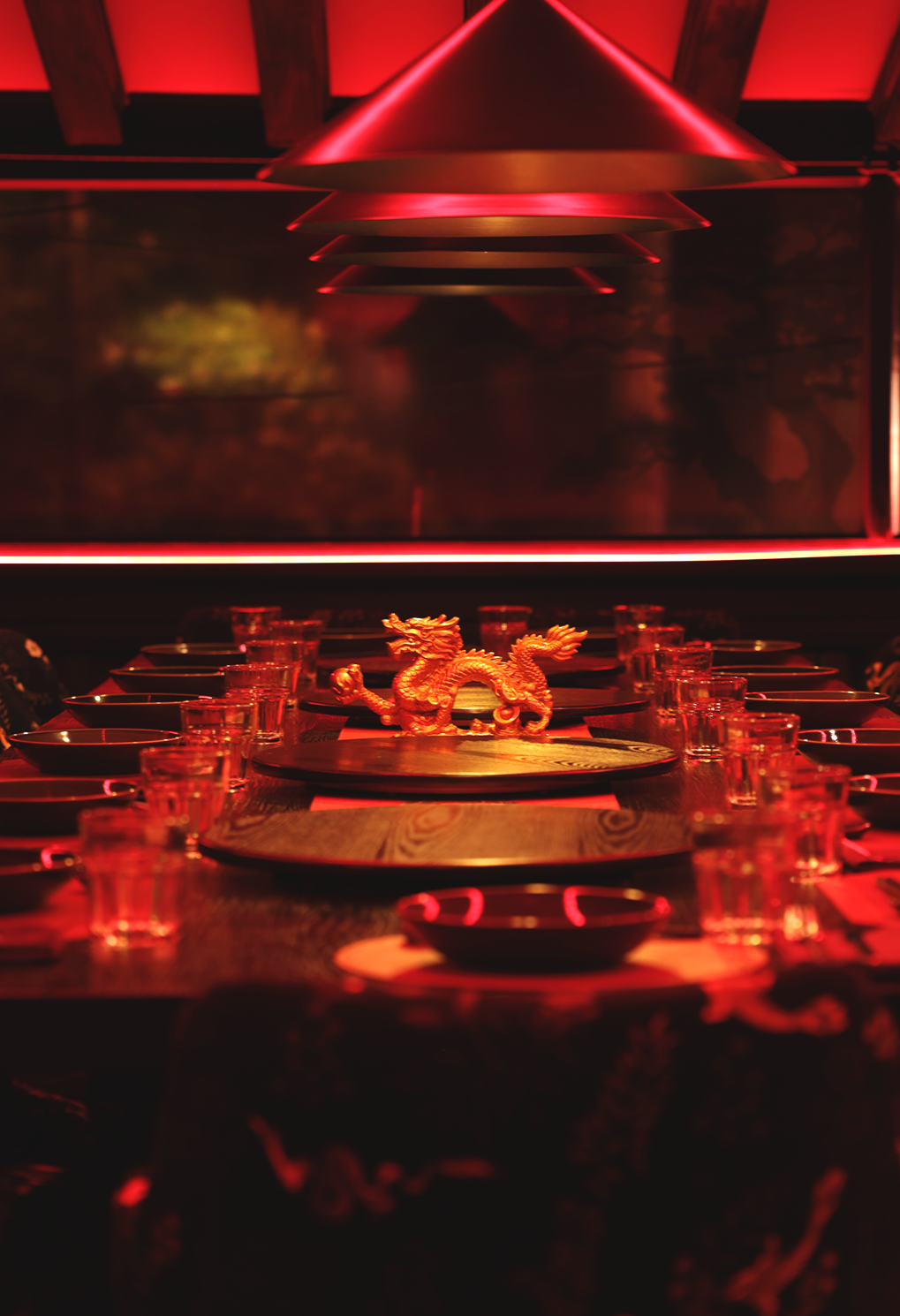 Red-lit dining table set for a banquet with a gold dragon centerpiece and glassware.