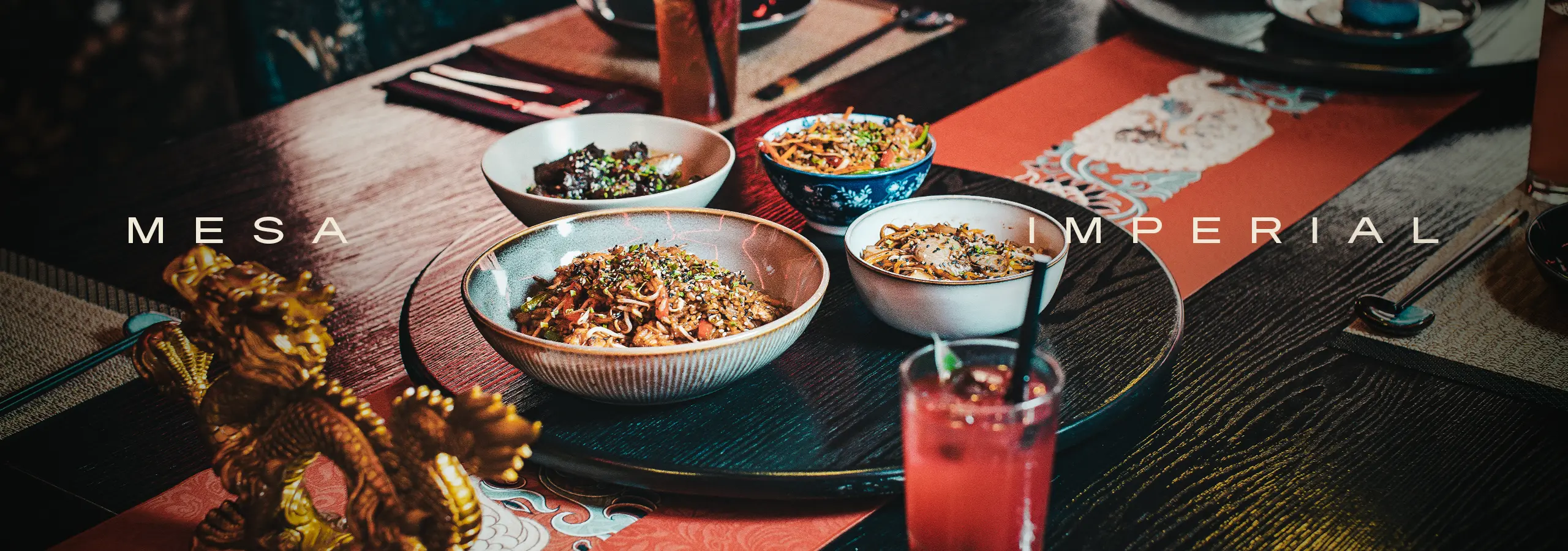 Assorted Asian noodle bowls on a dark wooden table with a red cocktail in the foreground and 'MESA IMPERIAL' branding across the image.